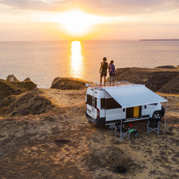 Aerial view of heterosexual couple on roof of camper van on seaside  at sunset
