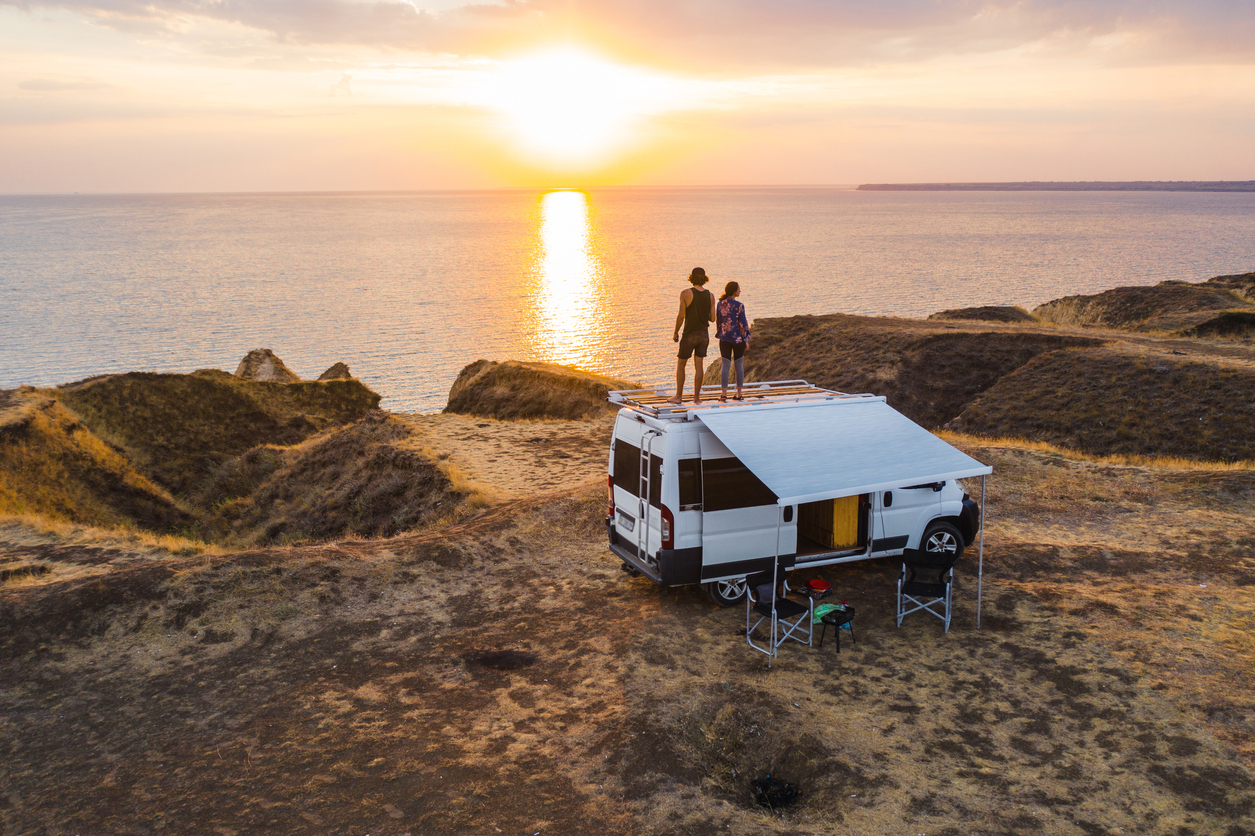 The Advantages and disadvantages of Buying New Electric Motor Residences for Sale Aerial view of heterosexual couple on roof of camper van on seaside  at sunset