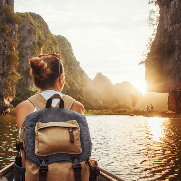 woman with backpack traveling by boat enjoying sunset among of mountains.
