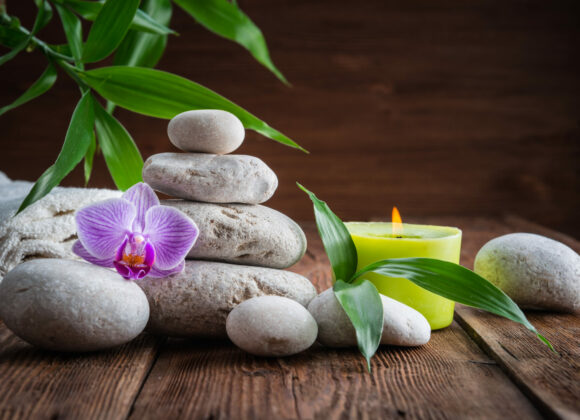 White Zen balance stones, an Orchid flower, a bamboo plant and a candle on a wooden table