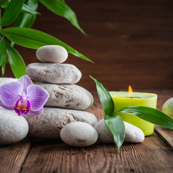 White Zen balance stones, an Orchid flower, a bamboo plant and a candle on a wooden table